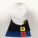 Berretto beanie in maglia, bianco con etichetta Boneswimmer a contrasto color porpora appoggiato su altri berretti in variante nera e blu