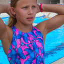 Modella bambina davanti alle corsie di una piscina con indosso il costume da allenamento nuoto Boneswimmer, modello intero PINUP 420pf con stampa di farfalle rosa fluo e azzurro