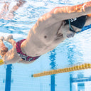 Un modello fotografato mentre nuota in piscina indossando il costume parigamba UCLA TRIBALE con un simpatico mostro in stile pop art